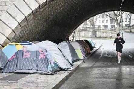  ?? MIGUEL MEDINA/AGENCE FRANCE-PRESSE ?? MAN runs past tents belonging to homeless migrants under the Sully bridge in the east of Paris, France.