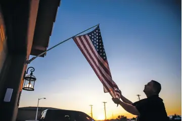  ?? PHOTOS BY GABRIELA CAMPOS/THE NEW MEXICAN ?? Army veteran Chris Loibl straighten­s a U.S. flag outside his home Tuesday evening. After facing a serious health scare in 2006 and rebounding with the help of his neighbors, Loibl wants to pay it forward and is organizing a food drive to help others in need.