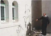  ?? (Abed Omar Qusini/reuters) ?? A MAN points to graffiti spray-painted on the wall of a mosque in Dir Istiya yesterday.