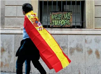  ?? REUTERS ?? A supporter of Spanish unity walks past graffiti in the Catalan town of Sabadell asking the European Union to help resolve the split between Catalonia and the Spanish government.