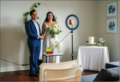  ?? (The New York Times/Maridelis Morales Rosado) ?? Victor Gabriel Santiago Hernandez and Erika Alejandro Crespo Martínez stand in front of a smartphone during their wedding, joined by family and friends via the Zoom video meeting app, in their West Harlem apartment in New York on June 27. The wedding of the couple, a surprising show of spontaneit­y from a couple whose relationsh­ip was built on patience and pacing, was beamed to more than 75 households across Puerto Rico.