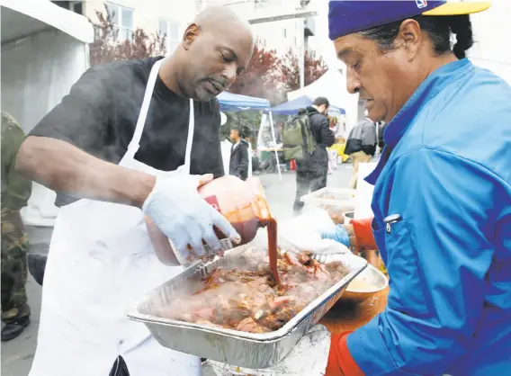  ?? Photos by Paul Chinn / The Chronicle ?? Charles Adams (left) and Jose Tovar finish a tray of pork ribs with barbecue sauce at the Black Cuisine Festival in San Francisco’s Bayview district.