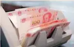  ??  ?? Chinese 100 yuan banknotes are seen in a counting machine while a clerk counts them at a branch of a commercial bank in Beijing, China. — Reuters
