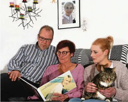  ?? RP-FOTO: EVERS ?? Guido, Heike und Mandy Hollands mit einem Buch, das zur Erinnerung an Kim gestaltet wurde. Auf Mandys Schoß sitzt Kater Urmel.