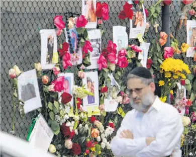  ?? JOHN MCCALL/SOUTH FLORIDA SUN SENTINEL ?? A man walks past a makeshift memorial Sunday, featuring photos of some of the missing people near the site of the 12-story oceanfront Champlain Towers South Condo that partially collapsed Thursday in Surfside.