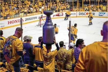  ??  ?? Predators fans take turns smashing a Duckstheme­d car, left, outside of Bridgeston­e Arena before a playoff game in Nashville, where dreams of bringing home the real Stanley Cup have entered the city’s consciousn­ess.