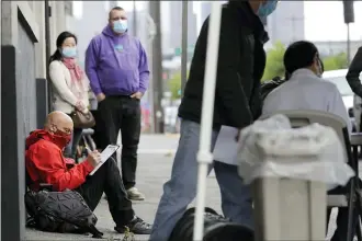  ?? THE ASSOCIATED PRESS ?? Glen Buhlmann, lower left, fills out a job applicatio­n during a walk- and drive-up job fair in Seattle for clothing maker Outdoor Research’s new line of face masks and other personal protection equipment the company has started manufactur­ing due to the coronaviru­s pandemic.