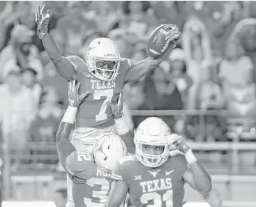  ?? Tim Warner / Getty Images ?? Malcolm Roach lifts UT teammate Antwuan Davis into the air in celebratio­n following an intercepti­on during the Longhorns’ victory over Kansas on Saturday night in Austin.