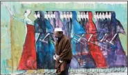  ??  ?? An Egyptian man passes by a mural and Arabic writing that reads, “Free men will continue the journey, coming back,” in Cairo Thursday.