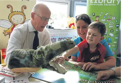  ??  ?? Deputy First Minister John Swinney plays with a crocodile puppet with David McKay and library outreach worker Alison Nolan as he takes part in a workshop at Newark Primary School, Port Glasgow, which is open during the summer as part of a special...