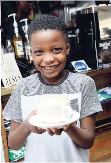  ??  ?? Eight-year-old Kahlil shows off his hot chocolate made by the Deaf Can! team at the E3 Cafe.