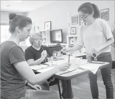  ?? Westside Eagle Observer/SUSAN HOLLAND ?? Wendzi Henzie (right) gives instructio­ns to students Kerrie Young and Paula Benson in an Asian Art class held at Henzie’s Art Studio Saturday, June 6. Students painted two watercolor paintings, did some Chinese calligraph­y, carved a stamp with their Chinese names to affix to their paintings and made some notecards using papercut designs. Upcoming sessions in the Gravette studio’s summer art camp workshops include classes on fantasy art, stamp making and green art.