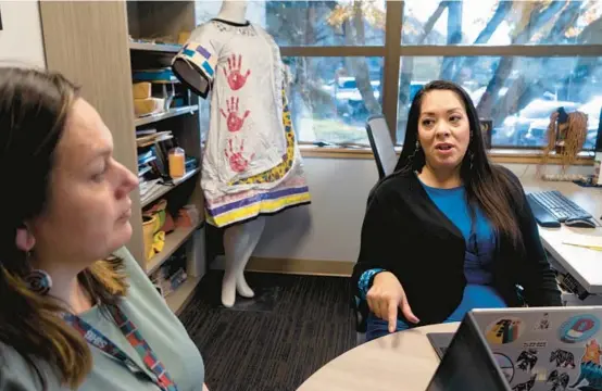  ?? RUTH FREMSON/THE NEW YORK TIMES ?? Abigail Echo-Hawk, right, speaks with a colleague in her office in front of a dress she constructe­d from body bags in Seattle. The dress, which evokes traditiona­l Native American ribbon dresses, incorporat­es red handprints, which are symbols of the Murdered and Missing Indigenous Women movement.