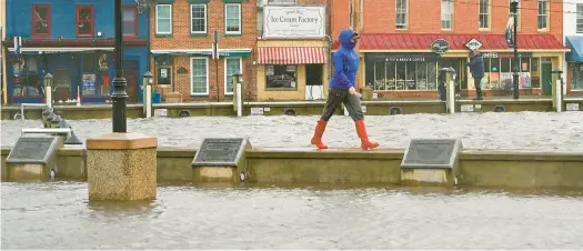  ?? PAUL W. GILLESPIE/CAPITAL GAZETTE ?? A pedestrian walks along the seawall at a flooded City Dock at high tide on Oct. 29, 2021.