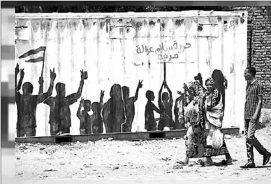  ??  ?? Civilians walk past graffiti reading in Arabic ‘Freedom, Peace, Justice and Civilian’ in the Burri district of Khartoum.
(Photo: Euronews)