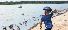  ??  ?? A kayaker paddles in Hyde Lake as Noah Allen, 6, throws a rock during a visit to Shelby Farms Park, which reopened following a $52 million improvemen­t project. YALONDA M. JAMES/THE COMMERCIAL APPEAL