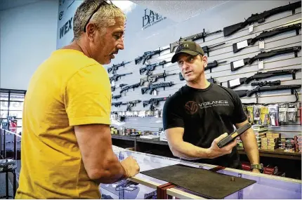  ?? BRUCE R. BENNETT / THE PALM BEACH POST ?? Brandon Wexler (right) of Wex Gunworks in Delray Beach shows his customized Glock to Rob Valente of Coral Springs at the store in late August. Business “has slowed down, but it’s not slow” since the election of Donald Trump, he said.