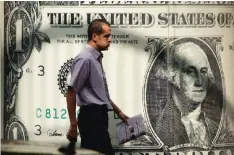  ?? — AP ?? CAIRO: A man walks past a poster showing a US dollar outside an exchange office in Cairo. President-elect Donald Trump’s ambitious plans to revive American exports, keep jobs in the United States and encourage oil drilling face a home-grown threat: the...