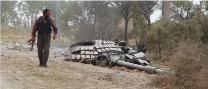  ?? -Reutes/Ammar Abdullah/File ?? WRECKAGE: A rebel fighter carries his weapon as he walks past the turret of a damaged tank at the Mastouma military base, after they seized it, in Idlib May 20, 2015.