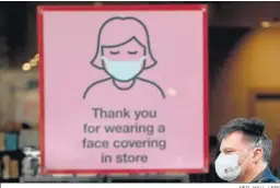  ?? NEIL HALL / EFE ?? Un hombre con mascarilla pasa ante un cartel que recuerda sus uso en Londres.