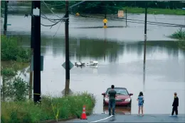  ?? CP PHOTO DARREN CALABRESE ?? People stand at the edge of floodwater near abandoned vehicles, following a major rain event in Halifax on July 22, 2023.