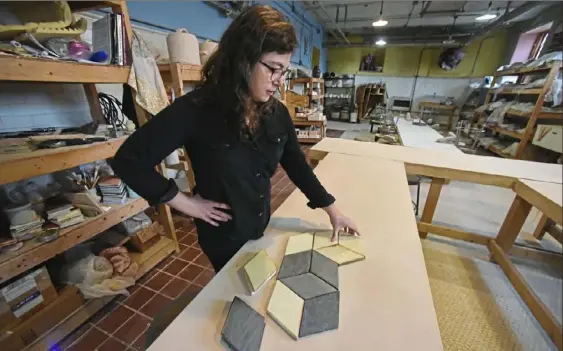  ?? Darrell Sapp/Post-Gazette ?? Katie Johnson, a consultant for Monmade’s expansion and a sculptor and potter who runs Braddock Tiles, arranges a pattern of tiles in the ceramics studio at Braddock's Carnegie Library.