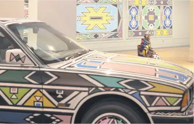  ?? Picture: AFP ?? FAMED. Influentia­l Ndebele artist Esther Mahlangu sits next to a BMW 525i covered in her artwork ahead of her major new retrospect­ive that opened at the Iziko South African National Gallery in Cape Town.