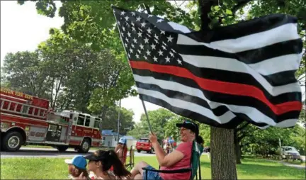  ?? TANIA BARRICKLO—DAILY FREEMAN ?? Gina Marino of Marlboro waves a flag firefighte­rs during the Ulster County Volunteer Firefighte­rs Associatio­n Parade Saturday afternoon as the parade marches by along Boice’s Lane in the town of Ulster, the location for this year’s parade. Seated with her are friends Sarah Wohlrab, left, and her sister Emily, 13, rear, whose father Timothy Wohlrab is a volunteer firefighte­r in Marlboro. In the foreground is Marino’s daughter Madylan, 14.