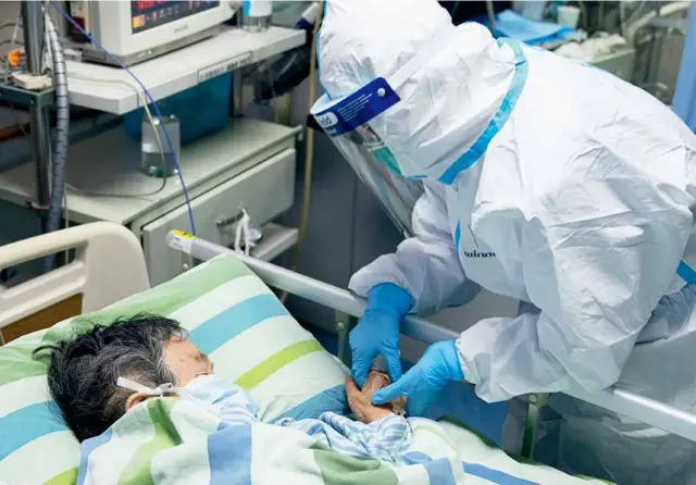  ?? 摄影 熊琦/新华社 ?? 2020年1月24日，武汉大学中南医院重症­隔离病房，护士长马晶一边握住病­人的手，一边安慰她。