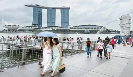  ?? AFP-Yonhap ?? People walk past the Merlion statue with the backdrop of the Marina Bay waterfront in Singapore, Jan. 3.