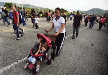 ?? REBECCA BLACKWELL AP ?? A woman pushes two children in a single stroller as migrants advance after Mexican police briefly blockaded the road, outside of Arriaga, Mexico on Saturday. Hundreds of Mexican federal officers carrying plastic shields blocked the caravan of Central American migrants from continuing toward the United States, after several thousand of the migrants turned down the chance to apply for refugee status and obtain a Mexican offer of benefits.