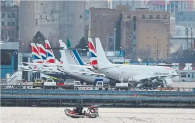  ?? Daniel Leal-Olivas, AFP ?? Bomb disposal workers in a boat pass grounded planes at London City Airport on Monday. Flights were canceled after a World War II bomb was found nearby in the River Thames.