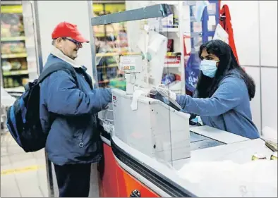  ?? PAU BARRENA / AFP ?? Una cajera con mascarilla y panel de protección en un supermerca­do de Barcelona