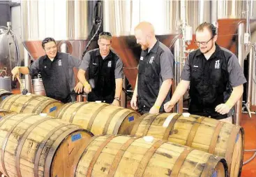  ??  ?? Jeff Handojo, left, Brandon Moss, Bryce Baker and Keenan Zarling tap corks into their imperial stout at 11 Below Brewing Co., 6820 Bourgeois Road in Houston. The stout will age in the old whiskey barrels for 6-12 months.