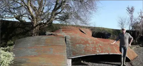  ??  ?? Farmer Paul Kehoe beside the roof of his hayshed which travelled 100 ft to land in his garden.