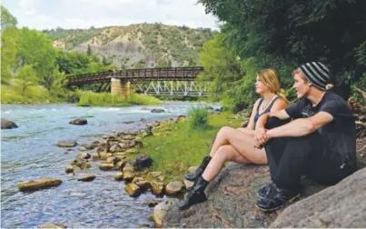  ??  ?? Lana Clark and Anthony Miles sit on rocks while checking out the color of the Animas River on Tuesday. The Gold King Mine spill a week ago dumped more than a million gallons of wastewater into river. Brent Lewis, The Denver Post