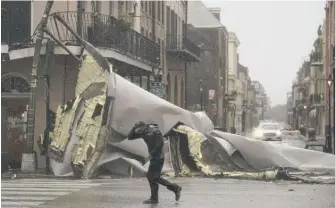  ?? ERIC GAY/AP ?? A man passes by a section of roof that was blown off of a building in the French Quarter of New Orleans by Hurricane Ida on Sunday.