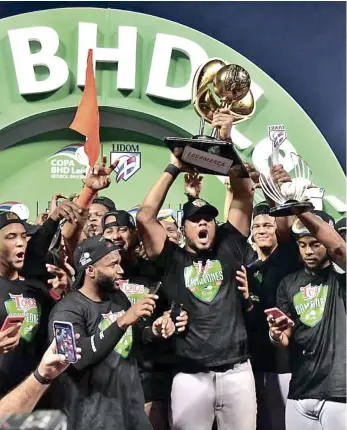  ??  ?? Jugadores festejan con la Copa BHD León que le acredita como los campeones y que le fue entregada por Jorge Besosa y José Sanoja, ejecutivos del banco BHD.