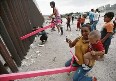  ?? Christian Chavez / Associated Press ?? A mother and her baby play on a seesaw installed within the steel fence that divides Mexico from the United States in Ciudad Juarez, Mexico. The architects also designed a gate to allow wlldlife to pass through.