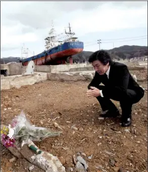  ?? AP/KOJI SASAHARA ?? Junzo Kumagai prays for his relative killed by a tsunami one year ago in the earthquake- and tsunami-devastated city of Kesennuma, Japan, on Sunday. In the distance is the 330-ton fishing vessel Kyotoku Maru No. 18, which was flung half a mile inland...