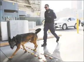  ?? Mario Tama / Getty Images ?? A Customs and Border Protection officer and his canine walk to inspect vehicles entering the United States at the San Ysidro port of entry on Monday in San Ysidro, Calif. President Donald Trump has issued a decree for the National Guard to protect the...