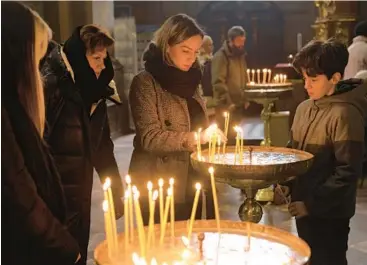  ?? SEAN GALLUP/GETTY ?? Natalya Nezhura, center, her children and mother light candles during a church service Friday in Lviv to honor her husband, Andrii, who served in the Ukrainian armed forces and was killed in January fighting Russian troops in the east.