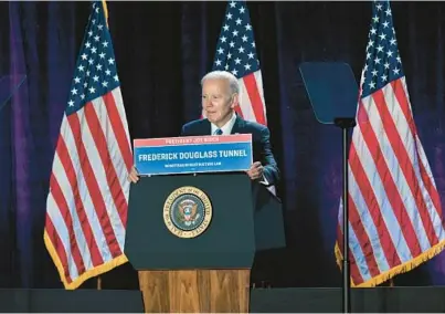 ?? KENNETH K. LAM/BALTIMORE SUN ?? President Joe Biden holds up a sign naming a tunnel in Baltimore after Frederick Douglass during his keynote address on the first night of the House Democratic Caucus Issues Conference at the Hyatt Regency Baltimore-Inner Harbor.