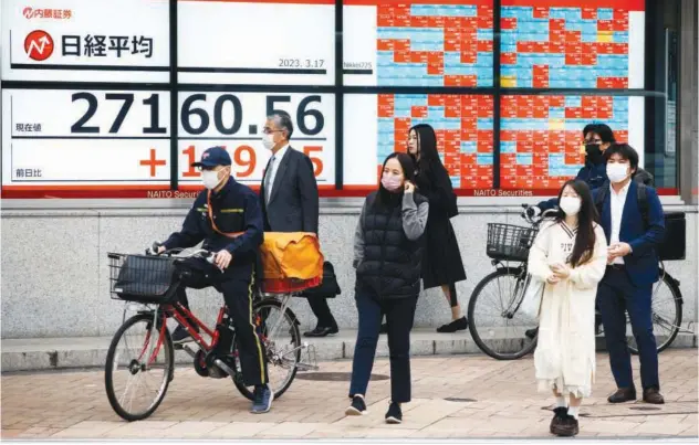  ?? Reuters ?? ↑
Passersby wait at a crossing in front of an electronic board showing Japan’s Nikkei average in Tokyo, Japan.