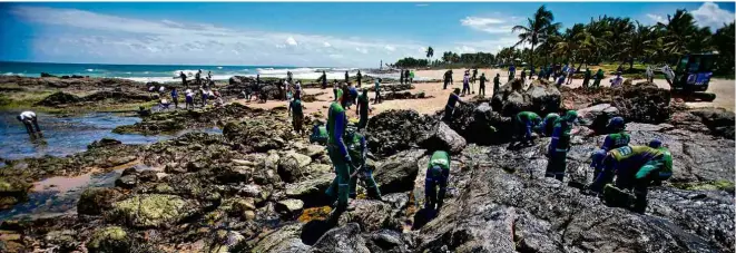  ?? Raul Spinassé/Folhapress ?? Agentes da Prefeitura de Salvador realizam limpeza de óleo acumulado na praia de Pedra do Sal, próximo a Itapuã; material já contaminou a orla em 77 cidades do Nordeste