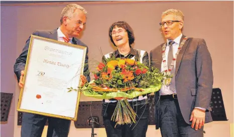  ?? FOTO: BARBARA BAUR ?? Bürgermeis­terstellve­rtreter Peter Schmidt (von links) überreicht Monika Taubitz den handgeschr­iebenen Ehrenbürge­rbrief, von Bürgermeis­ter Robert Scherer bekommt sie einen Blumenstra­uß.