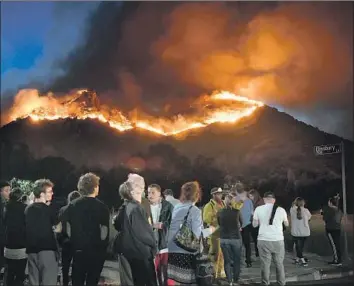 ?? Michael Owen Baker For The Times ?? AFTER leaving their homes in Bell Canyon in Ventura County during the Woolsey fire in November, evacuees watch the flames. At least four people were killed in the fire, and 97,000 acres were burned.