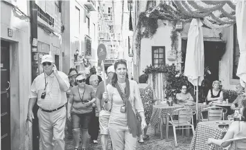  ??  ?? A tour guide leads a group of tourists through the streets of Alfama neighbourh­ood as locals sit at a terrace in Lisbon on July 2. The popular and most emblematic neighbourh­ood of the old Lisbon, Alfama, is now threatened by the influx of tourists...