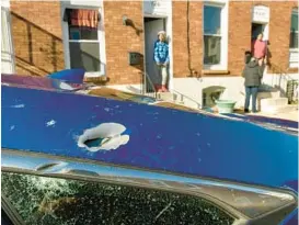  ?? ?? Above: A bullet hole shattered the window of a Honda Civic parked on the west side of the
700 block of North Glover Street, where a 17-year-old girl was killed in a double shooting Sunday.
A police officer holds a screen door open so a forensics technician can photograph details around the doorknob of a rowhouse.