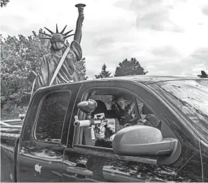  ?? NATHAN HOWARD/GETTY IMAGES ?? A member of the far-right group Proud Boys aims a paintball gun while leaving a demonstrat­ion with a Statue of Liberty replica in the bed of the truck on Aug. 22 in Portland, Ore. The Proud Boys and other far-right extremists fought with left-wing activists in Portland on the anniversar­y of a similar fight in 2020.